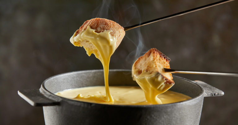 Dipping,Toasted,Bread,Into,A,Hot,Cheese,Fondue,Dripping,From